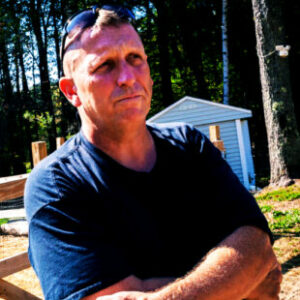 DV6 standing alone in the DV Farm fields wearing a black t-shirt and his sunglasses sitting atop his head.